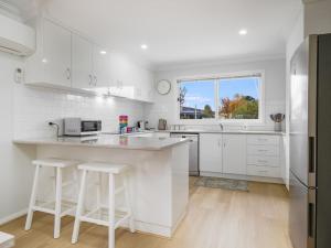 a white kitchen with a counter and stools in it at 61 Myack Street in Berridale
