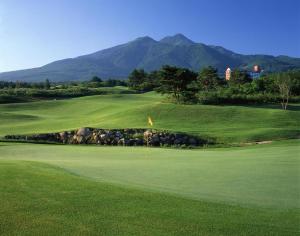 a green golf course with mountains in the background at Rockwood Hotel & Spa in Ajigasawa