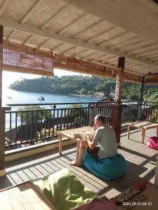 un hombre sentado en el suelo en un porche con vistas al agua en Dharma Yoga Homestay dan hostel, en Amed