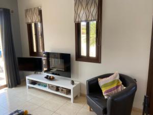 ein Wohnzimmer mit einem TV, einem Stuhl und einem Tisch in der Unterkunft Villa Kallista in Pissouri