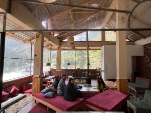 three people sitting on benches in a room with large windows at ThePahadians Food & Stay in Jibhi