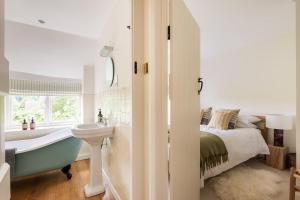 a bathroom with a bed and a sink and a bath tub at Architect Designed Cosy Cotswold Stone Cottage in Quenington