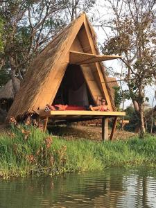 a woman laying on a bed in a doghouse by the water at Tad Lo Fandee Island - Bolaven Loop Pakse in Ban Kiangtat