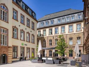 a group of buildings with tables and umbrellas at Ibis Styles Trier City in Trier
