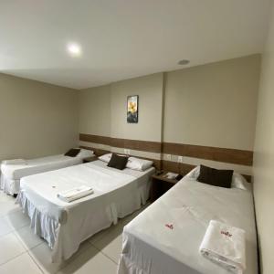 um quarto de hotel com duas camas com lençóis brancos em Onix Hotel Aeroporto em Lauro de Freitas