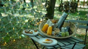 a picnic table with a basket of food and orange juice at Ô Pays Des Bois - Bulles et logements insolites en pleine nature - Adults Only in Parmilieu