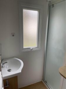 La salle de bains blanche est pourvue d'un lavabo et d'une fenêtre. dans l'établissement Mobil home 6/8 personnes, à Longeville-sur-Mer