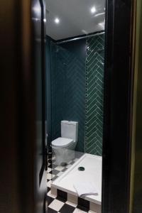 a bathroom with a toilet and a green tiled wall at Sleep at 55 in Tarporley