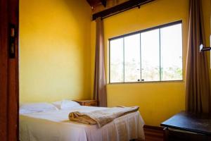 um quarto amarelo com uma cama e uma janela em Casa do Vaz - 3 opções de hospedagem na Lapinha da Serra! em Santana do Riacho