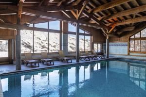 a swimming pool in a building with chairs and windows at Belambra Clubs Résidence Les Menuires - Le Hameau Des Airelles in Les Menuires