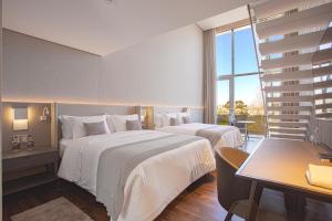 a hotel room with two beds and a table and a desk at Suryaa Hotel Pinhais, Curio Collection by Hilton in Pinhais
