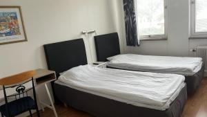 Duas camas num pequeno quarto com uma mesa e uma cadeira. em Drottninggatans Vandrarhem em Karlskrona