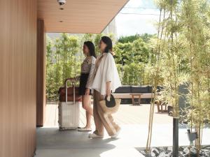 広島市にあるFAV HOTEL HIROSHIMA STADIUMの二人の女性が荷物を持って玄関に立っている