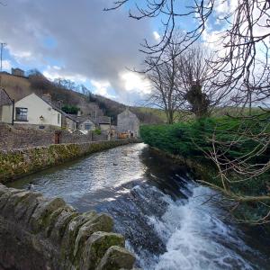 a river with a stone wall next to a river with waterfalls at Beech croft holiday cottage in Castleton
