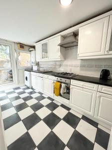 een keuken met witte kasten en een zwart-wit geruite vloer bij Lovely 2-bed 20 mins to central London in Londen