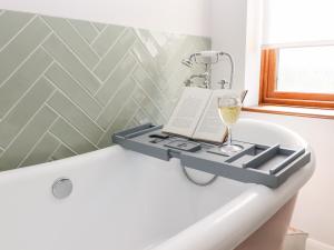 a bathtub with a glass of wine and a book at Baa Lamb Cottage in Burmarsh