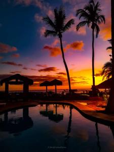 puesta de sol en la playa con piscina y palmeras en Barequeçaba Praia Hotel, en Barequeçaba