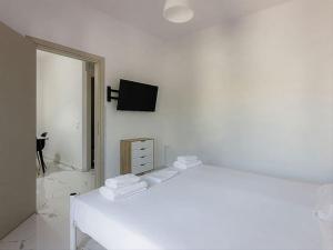 1 dormitorio blanco con 1 cama y TV en la pared en Hersonissos Modern One Bedroom Apartment Beachside, en Hersonissos