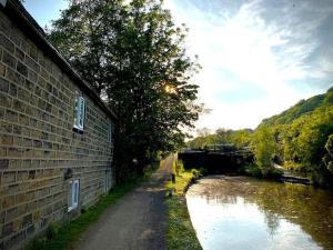 a dirt road next to a brick building next to a river at Cosy cottage with a canal view in Hebden Bridge