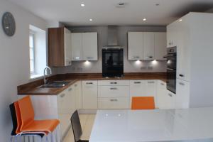 a kitchen with white cabinets and a table with orange chairs at The Silverstone House. Comfort, Convenience and no hassle at the doorstep of Silverstone Race Circuit. in Silverstone