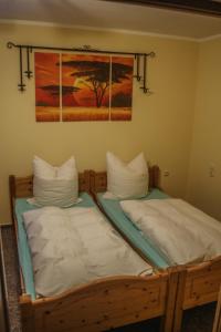 2 Betten mit weißen Kissen und ein Gemälde an der Wand in der Unterkunft Pension Muldental Großbothen Wohnung 1 in Grimma