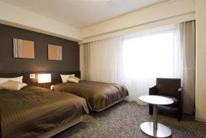 Cette chambre d'hôtel dispose de deux lits, d'une chaise et d'une fenêtre. dans l'établissement Dormy Inn Hakata Gion, à Fukuoka