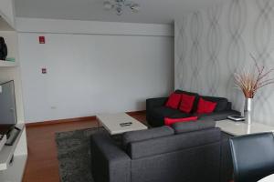 ein Wohnzimmer mit einem schwarzen Sofa und roten Kissen in der Unterkunft Elegante Flat en inmejorable ubicación - San Isidro in Lima