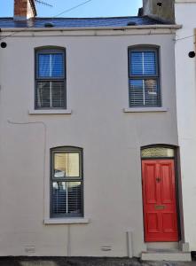 a white house with a red door and three windows at Violet House in Derry Londonderry