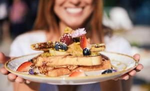 a woman holding a plate of food with fruit on it at Rhapsody Resort - Official in Gold Coast