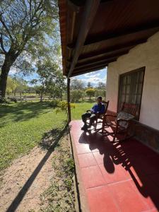 a man sitting on a bench on the porch of a house at EL PASO IBERA in Colonia Carlos Pellegrini