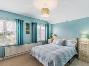 a blue bedroom with a bed and two windows at Dunlin in Burnham on Sea