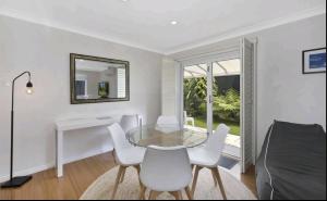 a dining room with a glass table and white chairs at Beachside Villa Ettalong Beach in Ettalong Beach