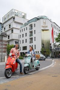 two people riding on scooters on a city street at HasHotel in Hasselt