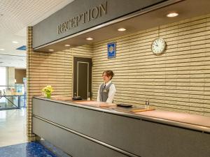 a woman standing at a reception counter in a lobby at Tokai City Hotel in Tokai
