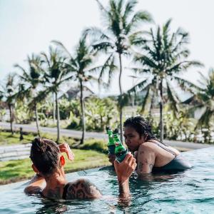 dos personas en la piscina bebiendo cerveza en Swell Hotel, Pool Bar & Restaurant, en Tanah Lot