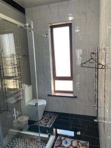 uma casa de banho com um chuveiro, um WC e uma janela. em KERUEN SARAY APARTMENTS 27/2 em Türkistan
