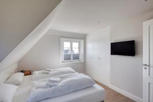 a white bedroom with a bed and a television at Rantum Dorf - Ferienappartments im Reetdachhaus 3 & 4 in Rantum