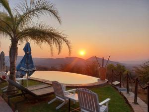 einen Pool mit zwei Stühlen und einer Palme und dem Sonnenuntergang in der Unterkunft Opuwo Country Lodge in Opuwo