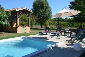 a swimming pool with chairs and an umbrella and a table at Ferme de Mouline in Sainte-Foy-la-Longue