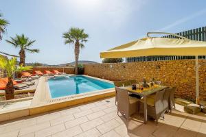 patio con tavolo, ombrellone e piscina di Tfiefa Holiday Home a Xagħra