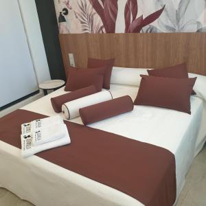 Cama grande con sábanas y almohadas marrones y blancas en Urbanlux Olimpia Superior en Albacete