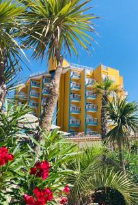 un edificio amarillo con palmeras delante en Hotel Capri 3 Stelle SUPERIOR, en Lido di Jesolo