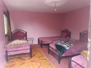 Cette chambre comprend 3 lits avec des murs roses et un tapis. dans l'établissement Auberge lac d'ifni, à Aoulouz