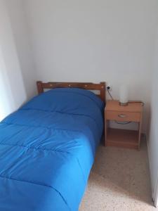 a bed with a blue comforter and a side table at Apartamentos Can bruguera 3 in Mataró