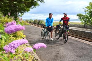 two men riding bikes on a road next to train tracks at Kents Bank Holiday - Pet Friendly with Bay Views in Grange Over Sands