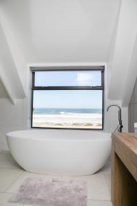 a large white bath tub in a bathroom with a large window at The Duinhuis Yzerfontein in Yzerfontein +38 photos
