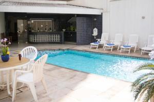 a swimming pool with white chairs and a table and a table and chairs at Mariano Palace Hotel in Campinas