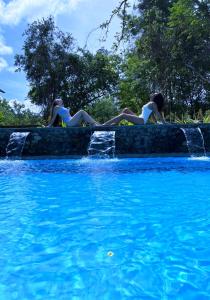 two women laying on a wall next to a swimming pool at Habarana Tree House Ambasewana Resort in Habarana