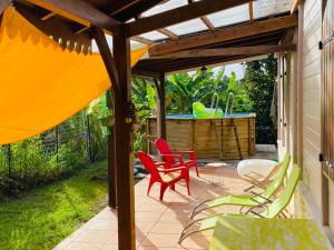 une terrasse avec des chaises rouges et vertes et un bain à remous dans l'établissement Magnifique Lodge en bois avec piscine et jardin de 800 m2, au Lamentin
