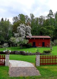 een rode schuur in het midden van een tuin met een hek bij Stunning Tiny House Tree of Life at lake Skagern in Finnerödja